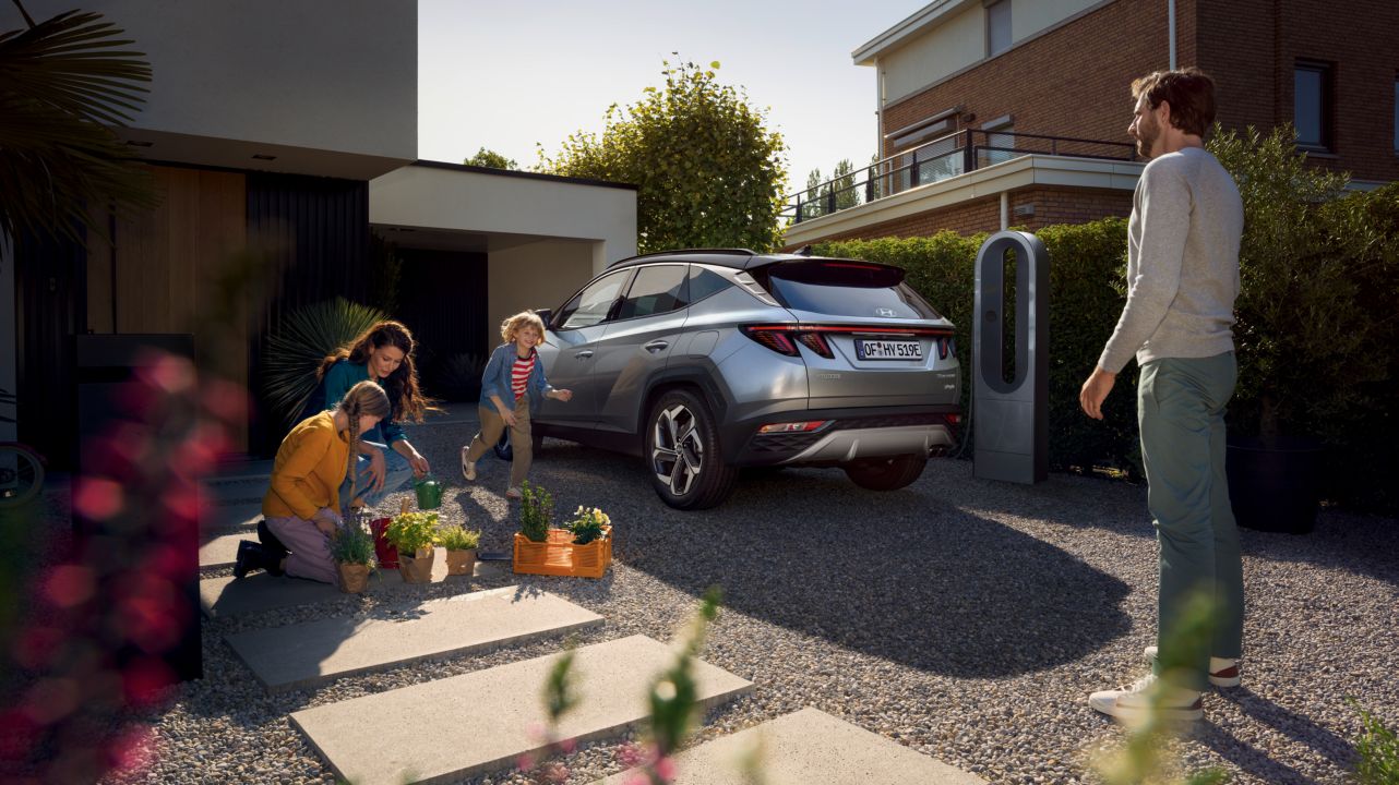 Zcela nové kompaktní SUV Hyundai TUCSON Plug-in Hybrid, zaparkované před domem s rodinou.